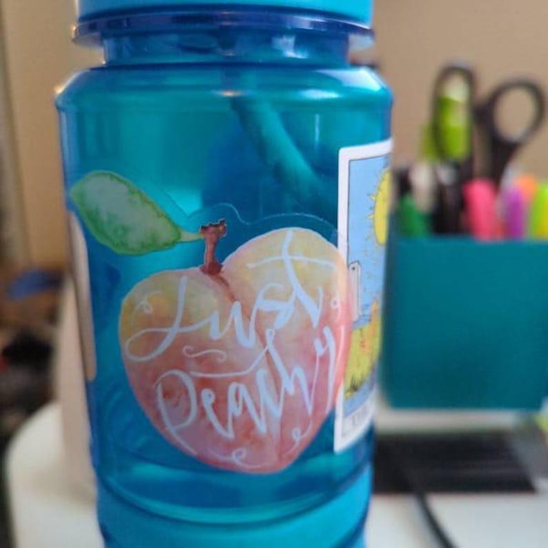 Op de afbeelding: Een blauwe herbruikbare waterfles met een sticker van een perzik waarop "Just Peachy" staat.