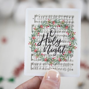 May include: A white sticker with a floral wreath and the text "O Holy Night" printed on a vintage sheet music background.