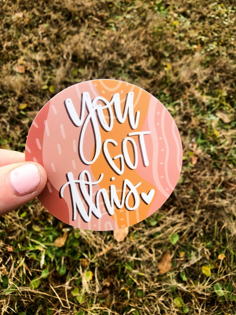 May include: A round sticker with an abstract design in shades of pink and orange. The sticker features white text that reads "You got this" with a small heart symbol.