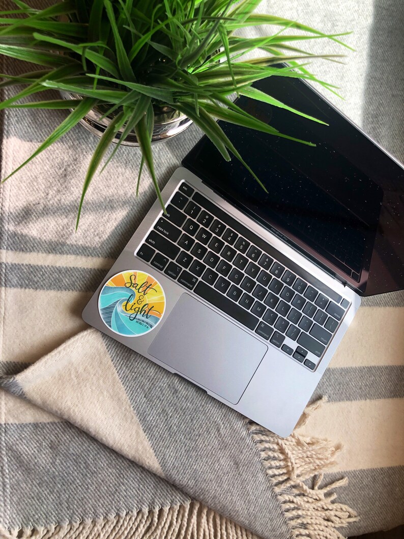 May include: A laptop computer with a sticker that says "Salt & Light" on a striped blanket. The sticker has a wave design and a yellow sun.