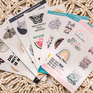 May include: A set of colorful sticker sheets with various designs and inspirational quotes. The stickers feature butterflies, rainbows, watermelons, and other cute illustrations. The quotes include "Treat people with kindness", "Choose gratitude", and "Every moment is a fresh begining".