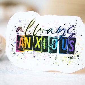 May include: White sticker with the words "always anxious" in black script and block letters. The word "ANXIOUS" is in rainbow colors. The sticker has a watercolor splatter effect.
