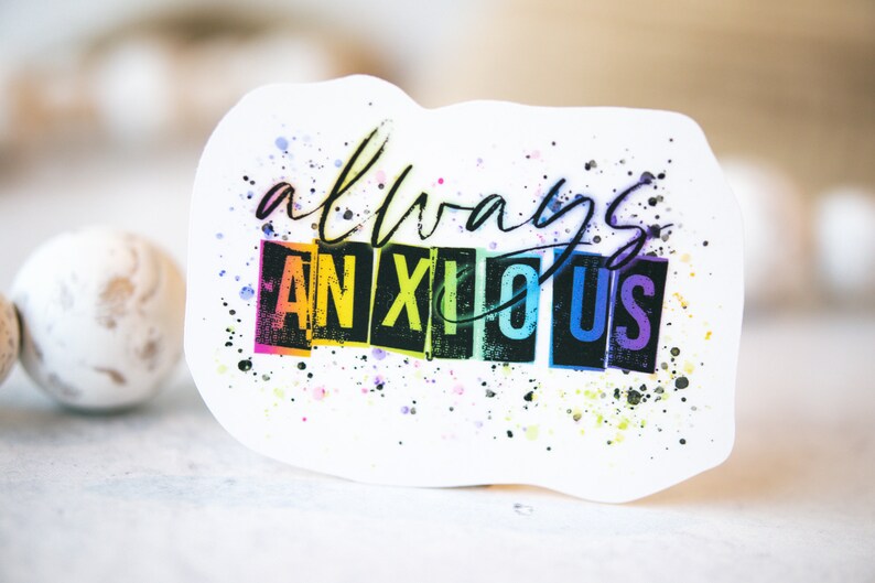 May include: White sticker with the words "always anxious" in black script and block letters. The word "ANXIOUS" is in rainbow colors. The sticker has a watercolor splatter effect.