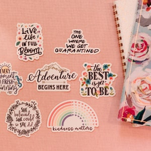 Puede incluir: Un conjunto de pegatinas coloridas con citas y dise&ntilde;os inspiradores. Las pegatinas presentan frases como "Vive la vida en plena floraci&oacute;n", "La aventura comienza aqu&iacute;", "Lo mejor est&aacute; por venir" y "La amabilidad importa".