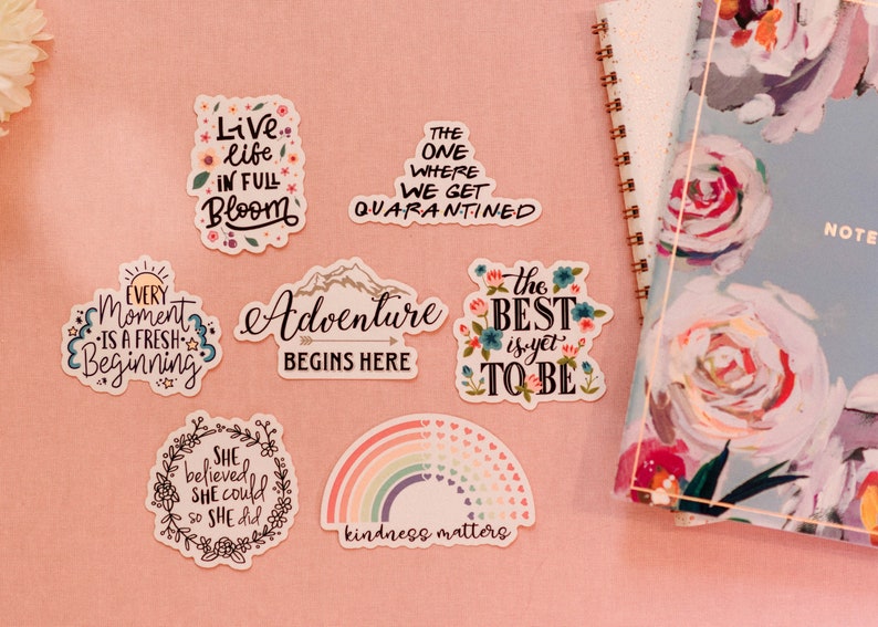 Puede incluir: Un conjunto de pegatinas coloridas con citas y dise&ntilde;os inspiradores. Las pegatinas presentan frases como "Vive la vida en plena floraci&oacute;n", "La aventura comienza aqu&iacute;", "Lo mejor est&aacute; por venir" y "La amabilidad importa".