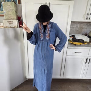 May include: A long-sleeved blue robe featuring a front zipper closure and a decorative embroidered panel around the neckline. The embroidery consists of floral patterns in shades of pink and white on a dark blue background.