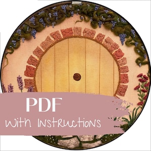 Può includere: Un cerchio da ricamo rotondo con un disegno ricamato a mano di una porta con una finestra rotonda. La porta è circondata da un bordo di ricamo rosa e marrone. Il cerchio è decorato con lavanda e altri fiori.