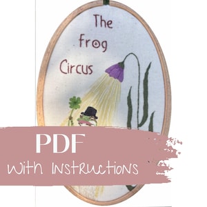 May include: Oval embroidery hoop featuring a whimsical frog circus design. The artwork includes a frog in a top hat, a purple flower, and the text "The frog Circus". The words "PDF with Instructions" are also visible.