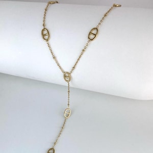 Peut inclure: Un collier lariat doré composé d'une chaîne fine ponctuée de cinq maillons ovales régulièrement espacés, chacun doté d'une barre horizontale centrale. Le design du collier présente une section en forme de Y qui pend verticalement.