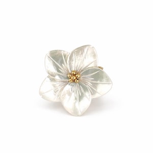 May include: A flower-shaped ring with five white petals and a cluster of small gold beads at the center. The ring is set against a white background, highlighting the delicate details of the floral design.