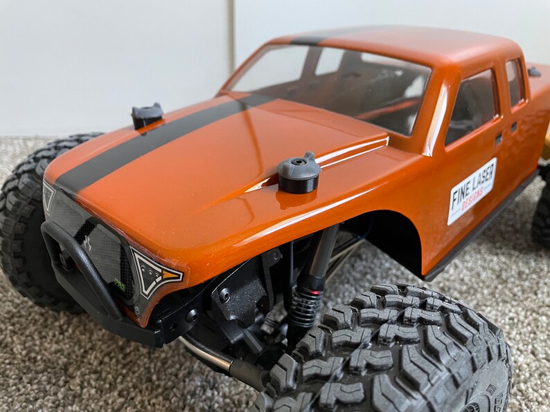 Pode incluir: Caminh&atilde;o RC personalizado de cor laranja e preta com uma faixa preta no cap&ocirc; e as palavras "FINE LASER DESIGNS" no lado.