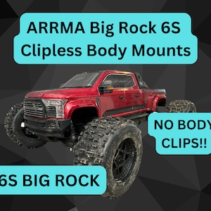 May include: Red and black remote control truck with large tires. The truck is labeled "ARRMA Big Rock 6S Clip less Body Mounts" and "6S Big Rock". The truck has a sign that says "NO BODY CLIPS!!"
