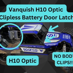 May include: A blue and white radio-controlled car with a black chassis and black wheels. The car has a white and blue Sparco sticker on the side. The car has a black latch on the battery door. The text "NO BODY CLIPS!!" is visible in the image.