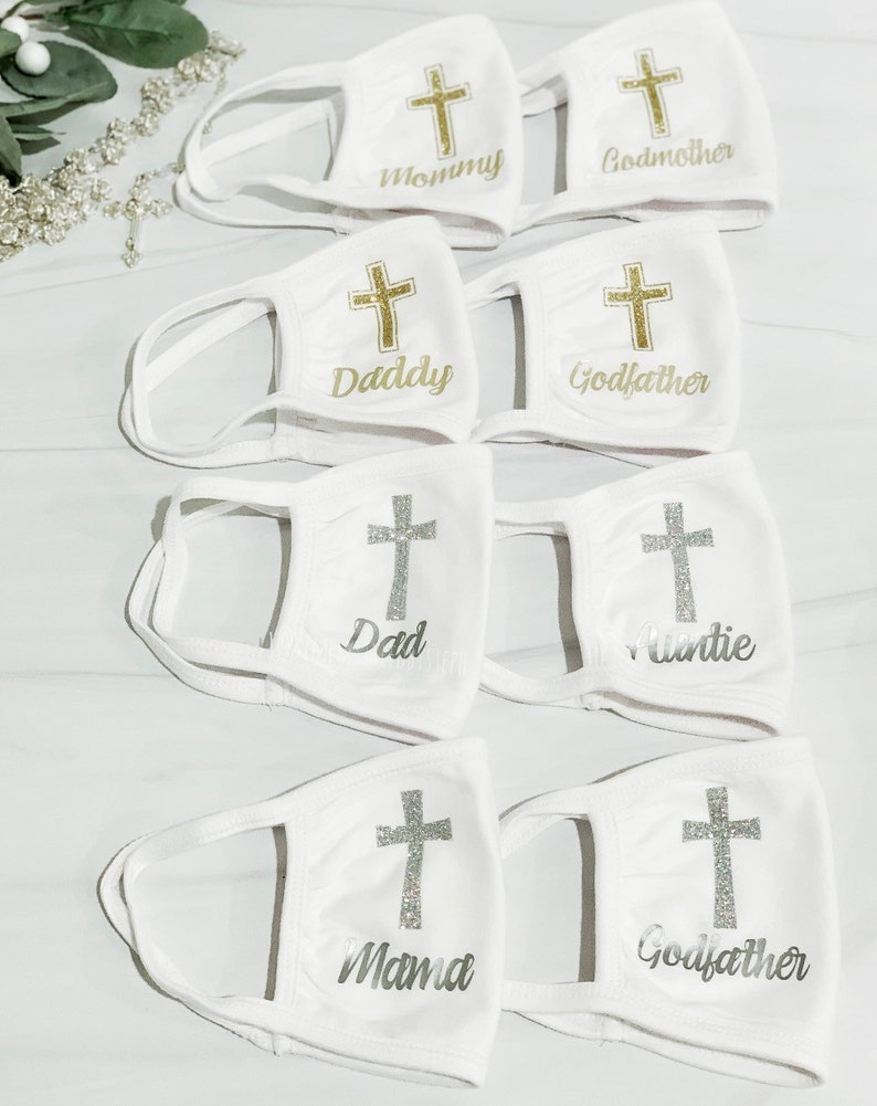 Op de afbeelding: Set witte gezichtsmaskers met een gouden kruis en een andere naam op elk masker. De namen zijn Mommy, Godmother, Daddy, Godfather, Dad, Auntie, Mama en Godfather.