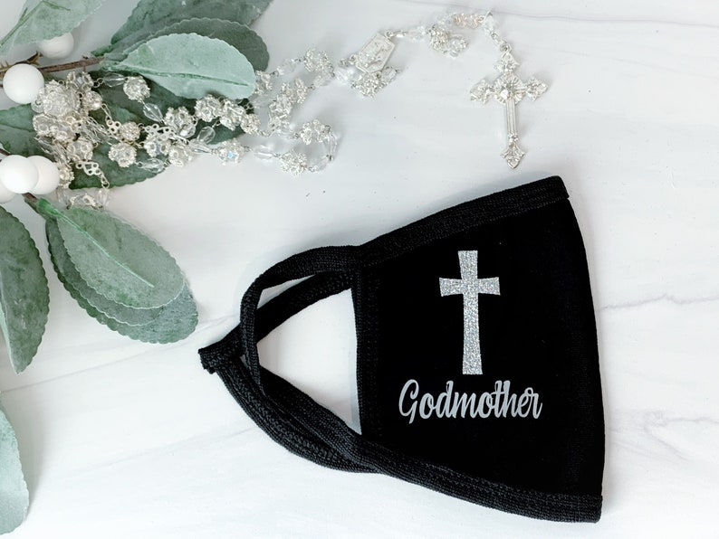 Op de afbeelding: Zwart mondkapje met een zilveren glitterkruis en het woord "Peetmoeder" erop gedrukt.