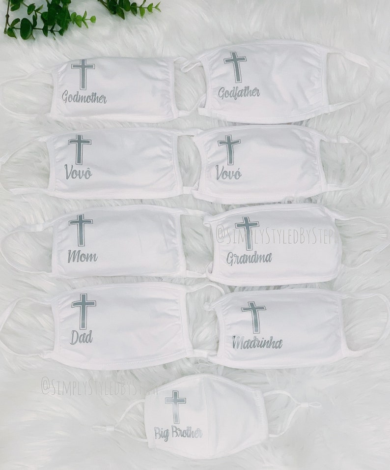 Op de afbeelding: Set witte gezichtsmaskers met een zilveren kruis en verschillende titels, waaronder "Peter", "Meter", "Vov&oacute;", "Moeder", "Vader", "Oma", "Peetmoeder" en "Grote broer".