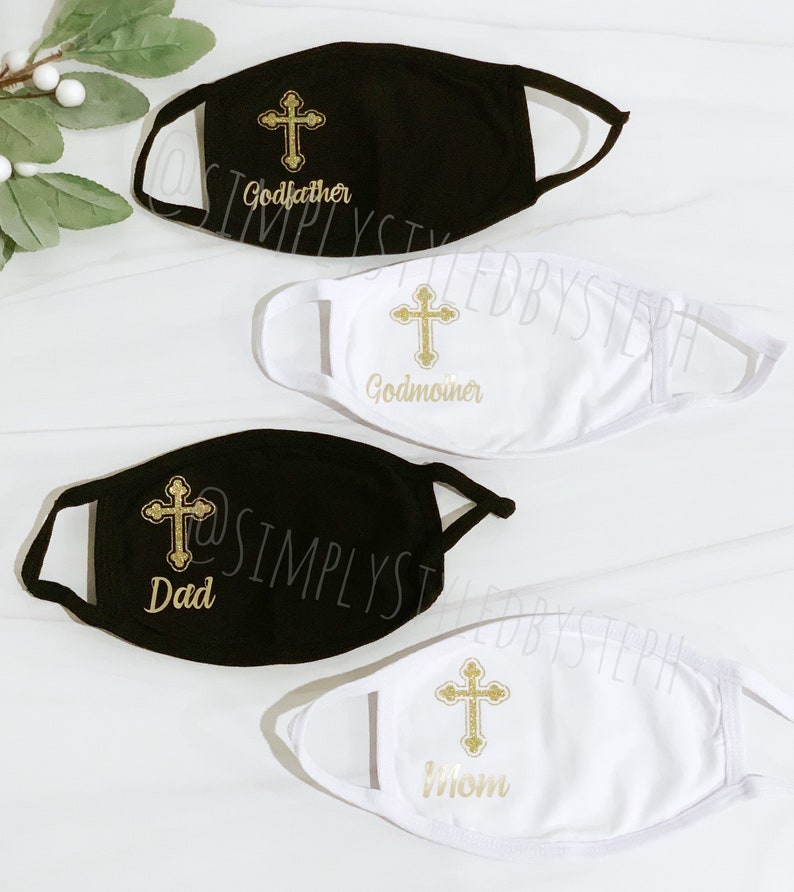 Op de afbeelding: Vier gezichtsmaskers met een gouden kruisontwerp en verschillende tekst. De maskers zijn wit en zwart. De tekst op de maskers luidt "Peter", "Peetmoeder", "Papa" en "Mama".