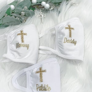 Op de afbeelding: Drie witte gezichtsmaskers met gouden glitterkruisen en gepersonaliseerde tekst. De maskers hebben de tekst "Mommy", "Daddy" en "Pablito".