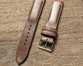 May include: A two-piece brown leather watch strap featuring a smooth finish, tonal stitching, and a polished silver-tone metal buckle. The longer piece includes six circular adjustment holes, while the shorter piece has two leather keepers.