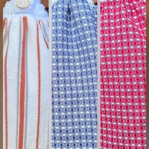 May include: Three hanging kitchen towels with crocheted white tops and wooden buttons labeled Handmade. The first towel features orange and gray vertical stripes on white. The second has a blue and white diamond pattern. The third has a red and white diamond pattern.