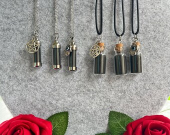 May include: A collection of necklaces featuring small, dark-colored vials and cylindrical pendants. Some pendants have silver chains and charms, including a pentagram and an evil eye. The necklaces are displayed against a gray background with red roses at the bottom.