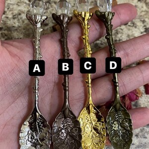 May include: Four decorative spoons with crystal-like tops and ornate floral designs. The spoons are in silver, bronze, gold, and antique brass. Each spoon has a different color and is labeled A, B, C, and D.