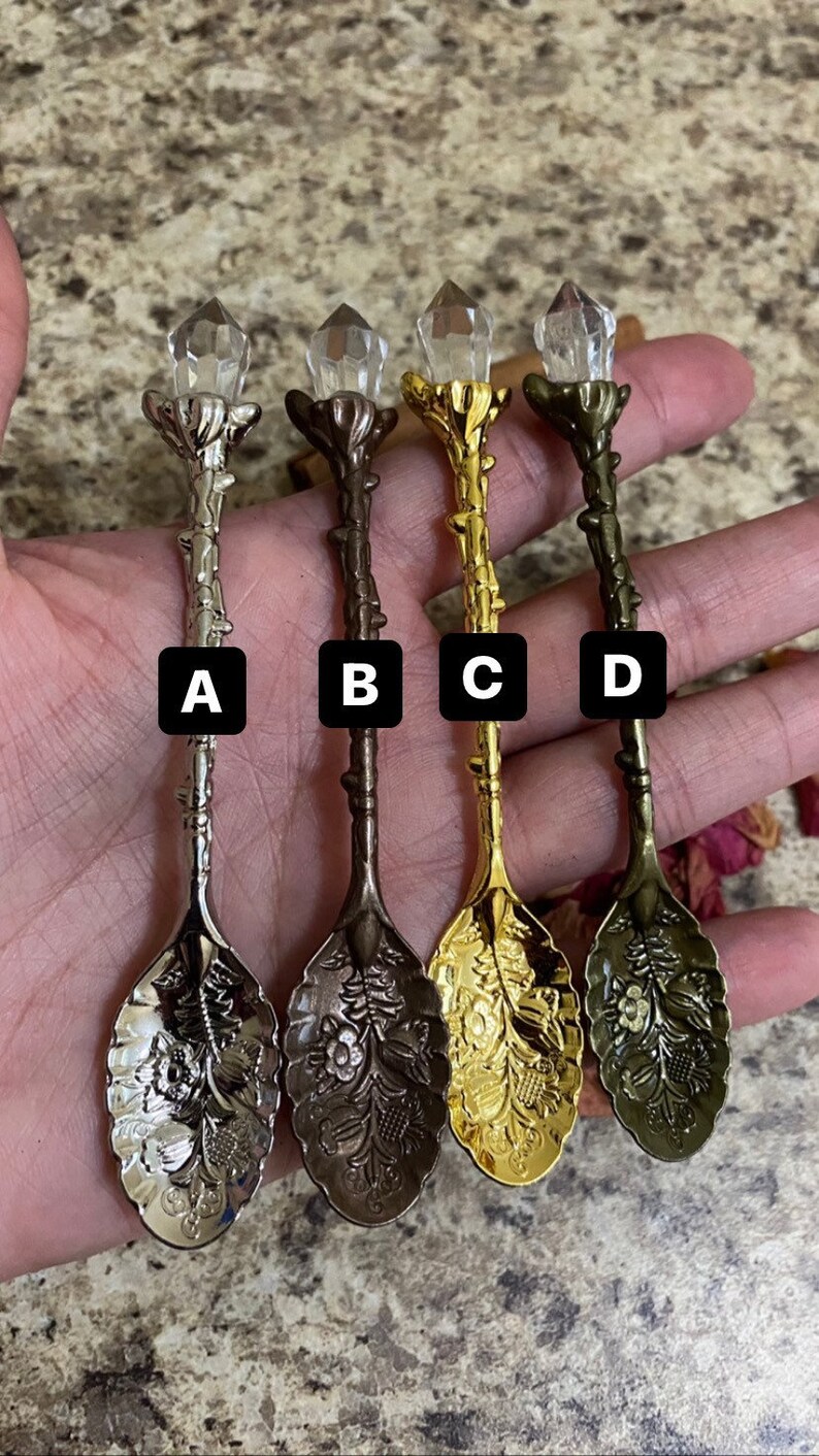 May include: Four decorative spoons with crystal-like tops and ornate floral designs. The spoons are in silver, bronze, gold, and antique brass. Each spoon has a different color and is labeled A, B, C, and D.