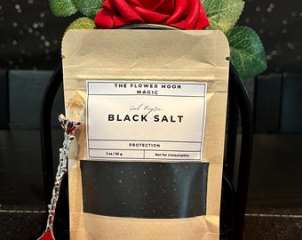 May include: A package of black salt with the text "BLACK SALT" and "PROTECTION". The package is adorned with a red rose and a decorative spoon. The label reads "THE FLOWER MOON MAGIC". The package contains 3 oz / 85 g of black salt.