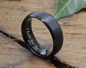 May include: A black tungsten carbide ring with a brushed finish and a beveled edge. The inside of the ring is engraved with the words "I Love You More".