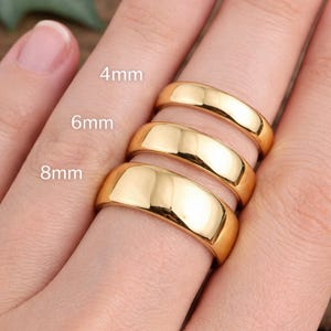 May include: Gold-colored rings in 4mm, 6mm, and 8mm widths are displayed on a finger. The rings have a polished, reflective surface. The image includes the text "4mm", "6mm", and "8mm".