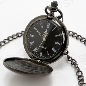 May include: A black pocket watch with a black chain and a white face with Roman numeral markings. The watch face says "QUARTZ".