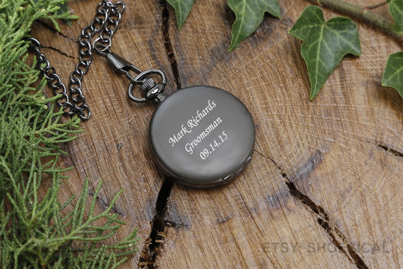 May include: A black pocket watch with a silver chain. The watch face is engraved with the text "Mark Richards, Groomsman, 09.14.15".