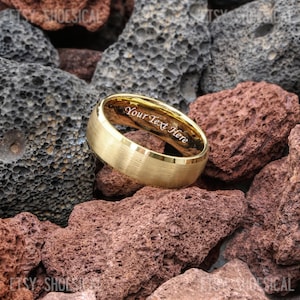 May include: A gold-toned ring with a brushed matte exterior finish and a polished interior band. The inner surface of the ring features the engraved text "Your Text Here" in a clear, sans-serif font, visible from the side angle.