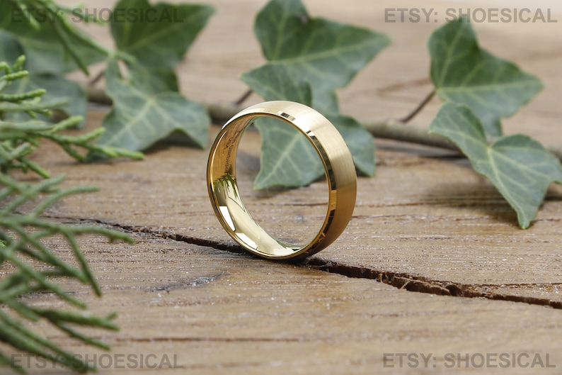 May include: A gold-colored metal ring with a smooth, polished finish and a slightly domed profile. The band features a reflective surface that catches the light, showing a bright, metallic luster throughout the circular design.