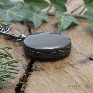 May include: A black pocket watch with a chain on a wooden surface. The watch has a silver finish and a hinged lid.