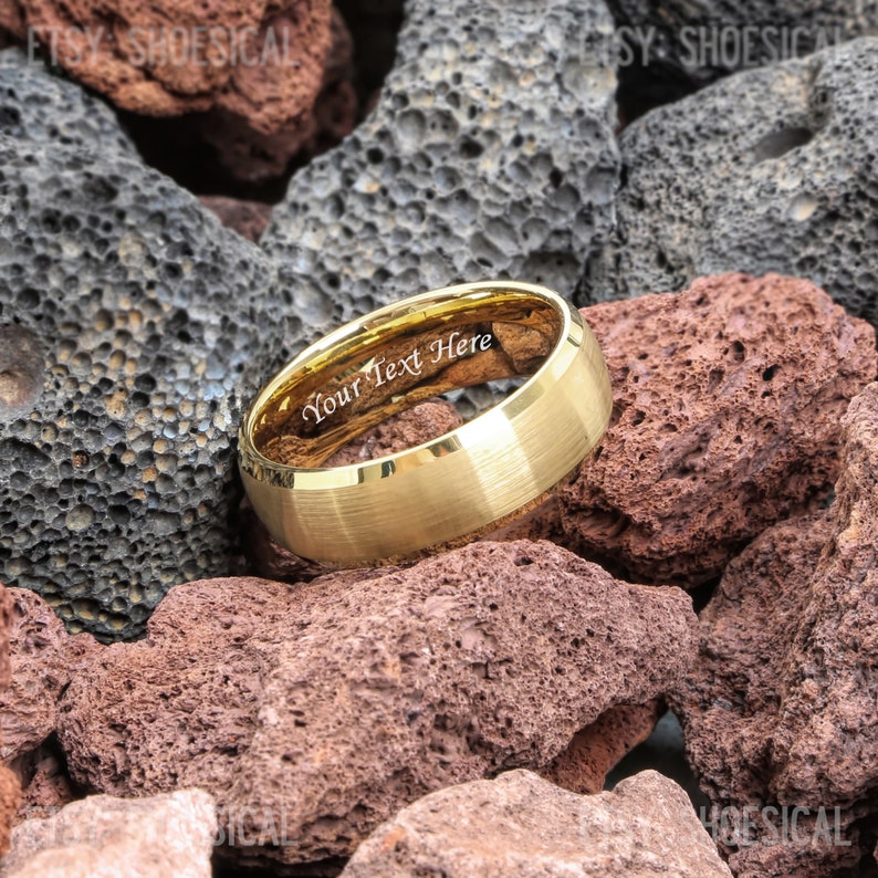 May include: A gold-toned metal ring with a brushed finish and a polished beveled edge. The interior of the band features the engraved text "Your Text Here" in a white serif font, visible against the reflective gold-colored inner surface.