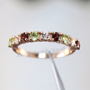 Peut inclure: Une délicate bague en or avec une rangée de pierres précieuses vertes, blanches et rouges alternées. La bague est sertie de petites pierres rondes.