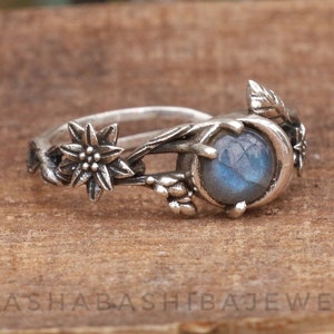 May include: A silver ring featuring a blue labradorite gemstone, set within a crescent moon design and surrounded by floral details.