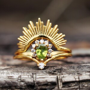 May include: Gold ring set with a pear-shaped green gemstone surrounded by smaller clear gemstones. The top ring features a sunburst design.