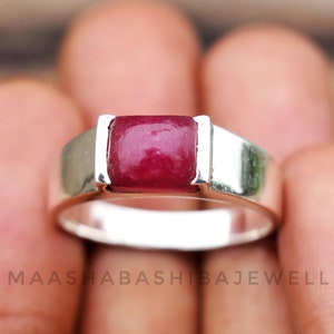 May include: A silver ring with a square-shaped red gemstone set in the center. The ring is simple and elegant.