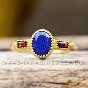 Peut inclure: Une bague en or avec une pierre ovale en lapis-lazuli bleu entourée d'une bordure perlée. Deux pierres de grenat rouge sont serties de chaque côté du lapis-lazuli.