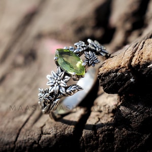 Könnte beinhalten: Ein silberner Ring mit einem grünen Edelstein und einem floralen Design. Der Ring liegt auf einer Holzoberfläche.