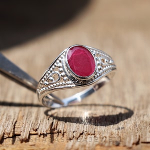 May include: A silver ring with a red oval gemstone set in a decorative band.