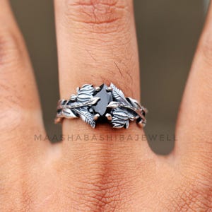 May include: A silver ring with a black gemstone set in a floral design. The ring is worn on a person's finger.