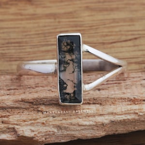 May include: A silver ring with a rectangular black and white dendritic agate stone set in a V-shaped band.