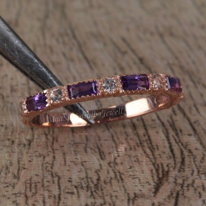 May include: A rose gold band ring with a row of alternating amethyst and white gemstones. The ring has a textured band and is set with rectangular-shaped amethysts.