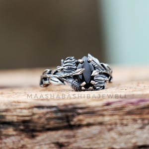 May include: A silver ring with a black gemstone surrounded by delicate silver leaves and branches.