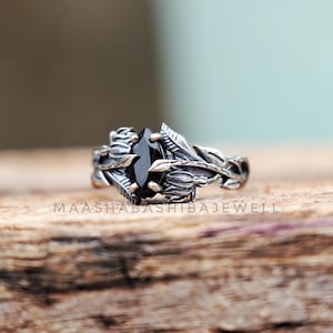 May include: A silver ring with a black gemstone set in a floral design. The ring features intricate details and a delicate, organic style.