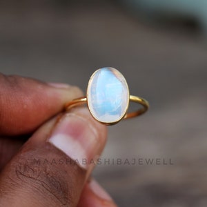 Op de afbeelding: Een gouden ring met een witte ovale maansteen. De ring is simpel en elegant.