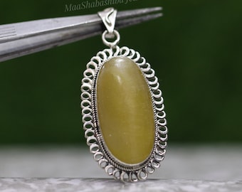 May include: An oval pendant featuring a smooth, light yellow stone set in a silver frame with a decorative scalloped edge and a twisted wire border. The pendant includes a silver bail at the top and displays the text MaaShabashibaJewell.